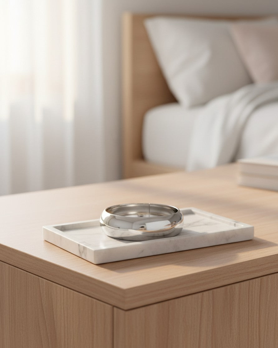 Elli Jewellery rhodium plated polished bangle bracelet resting on a white marble tray in a minimalist bedroom setting.