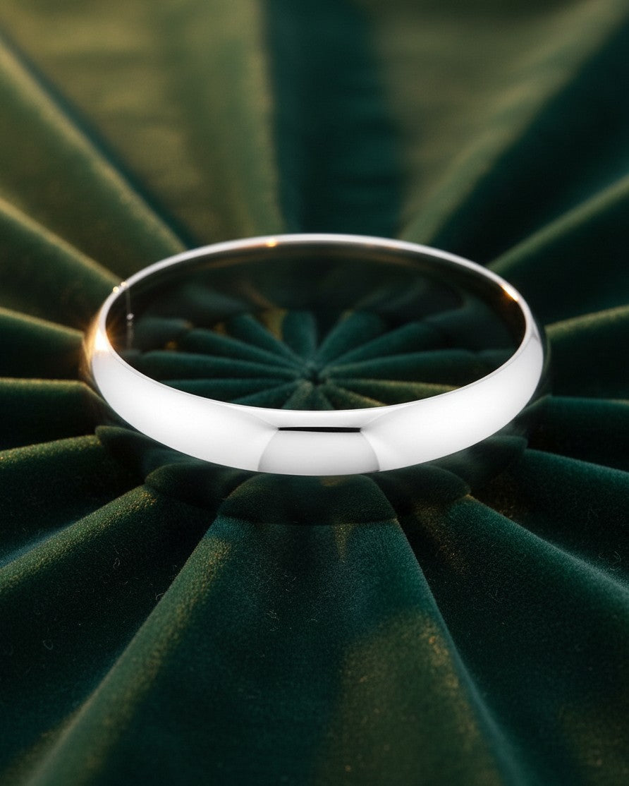 Elli Jewellery sleek rhodium plated bangle bracelet with a polished silver finish resting on a dark green velvet base.