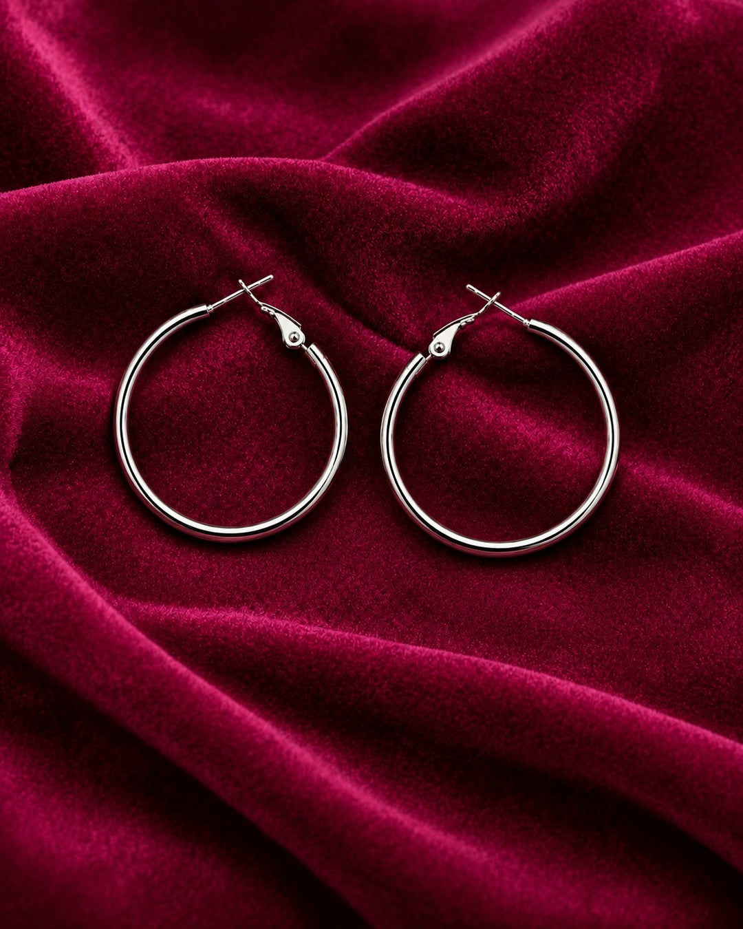 Elli Jewellery classic smooth rhodium plated hoop earrings with a polished silver finish on deep red velvet fabric.