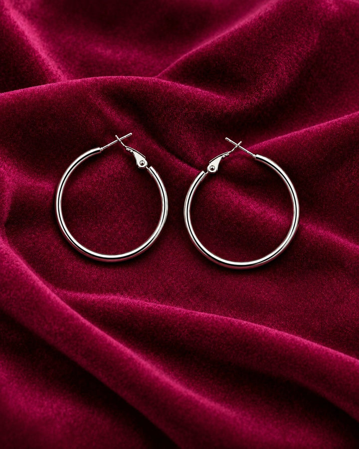 Elli Jewellery classic smooth rhodium plated hoop earrings with a polished silver finish on deep red velvet fabric.