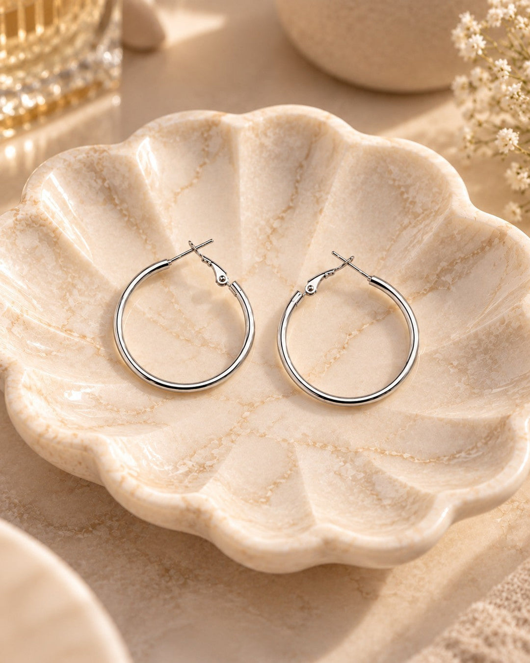 Elli Jewellery classic smooth rhodium plated hoop earrings in a polished silver finish resting on a shell dish
