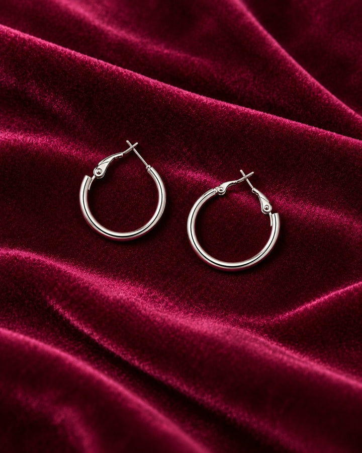 Elli Jewellery rhodium plated hoop earrings with a polished silver finish resting on a deep red velvet fabric.