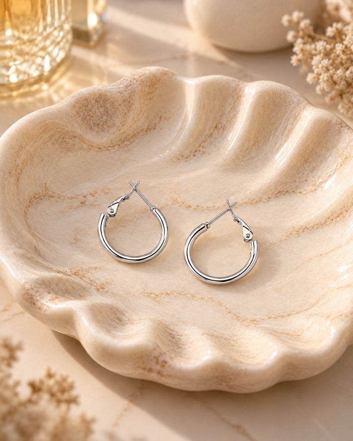Elli Jewellery classic rhodium plated hoop earrings with a polished silver finish resting on a decorative shell dish.