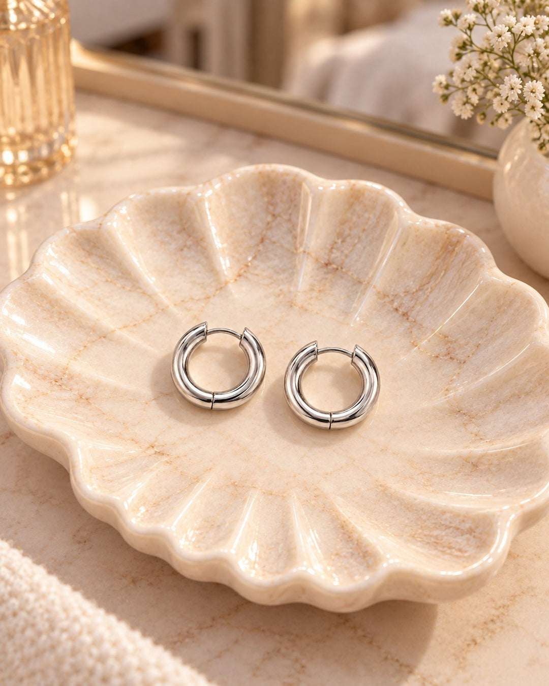 Elli Jewellery rhodium plated mid huggie hoop earrings resting on a decorative shell dish with a minimalist design.