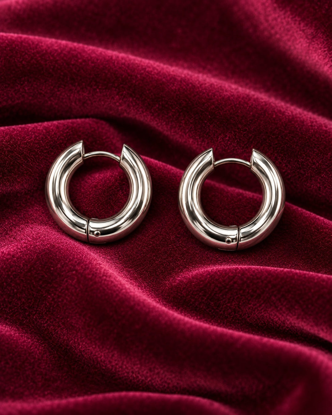 Elli Jewellery rhodium plated waterproof huggie hoop earrings with a polished silver finish on deep red velvet.