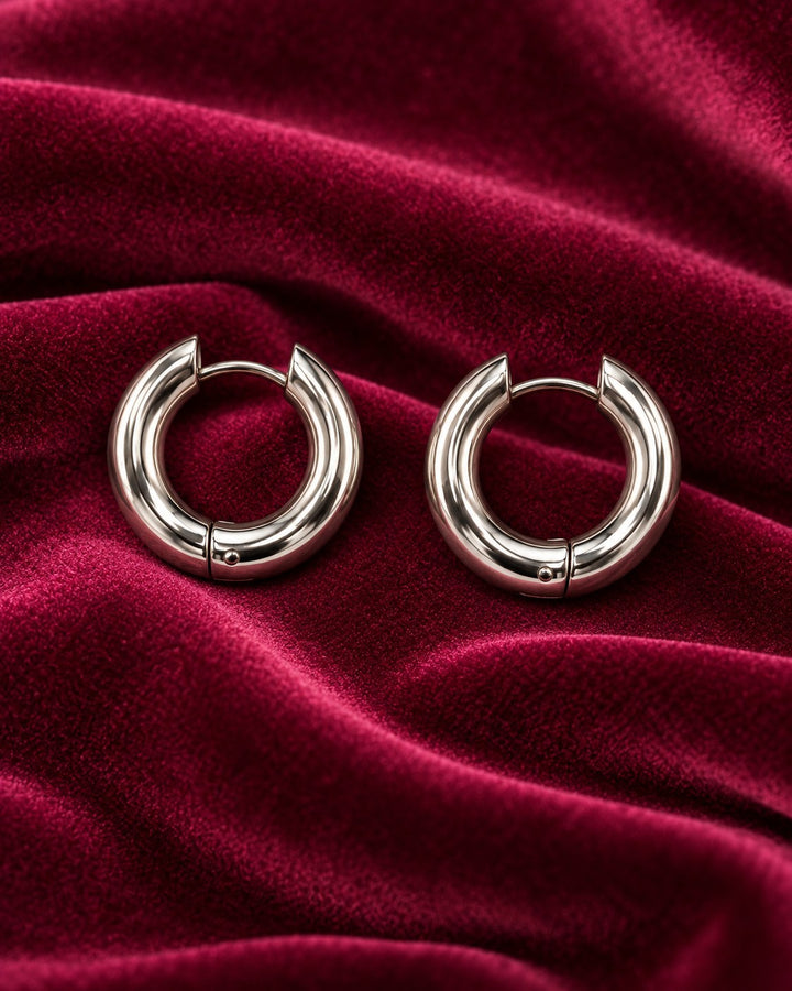 Elli Jewellery rhodium plated waterproof huggie hoop earrings with a polished silver finish on deep red velvet.