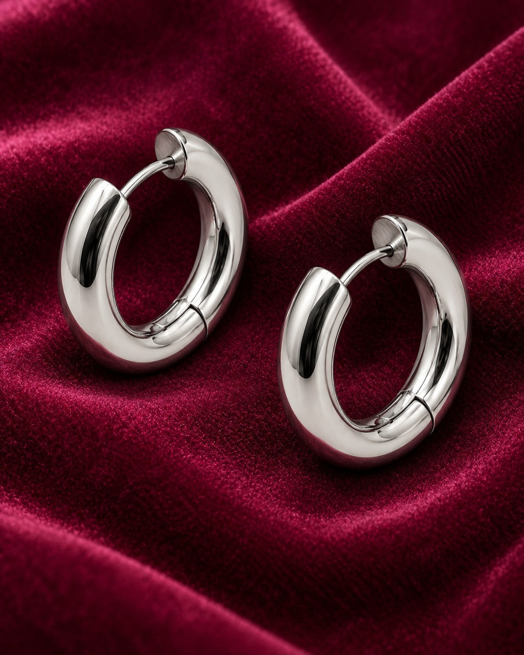Elli Jewellery rhodium plated waterproof mid huggie hoop earrings with a polished silver finish on red velvet fabric.