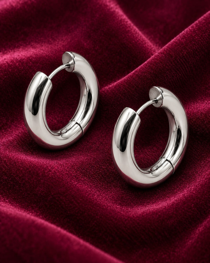 Elli Jewellery rhodium plated waterproof mid huggie hoop earrings with a polished silver finish on red velvet fabric.