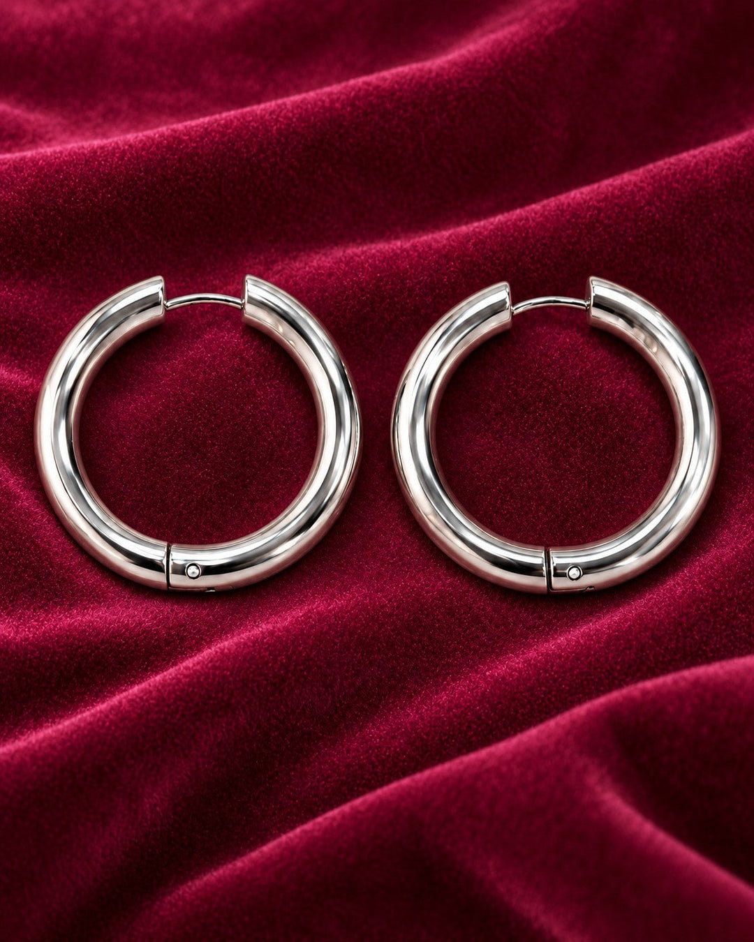 Elli Jewellery rhodium plated mid hoop earrings with a polished silver finish on a deep red velvet background.