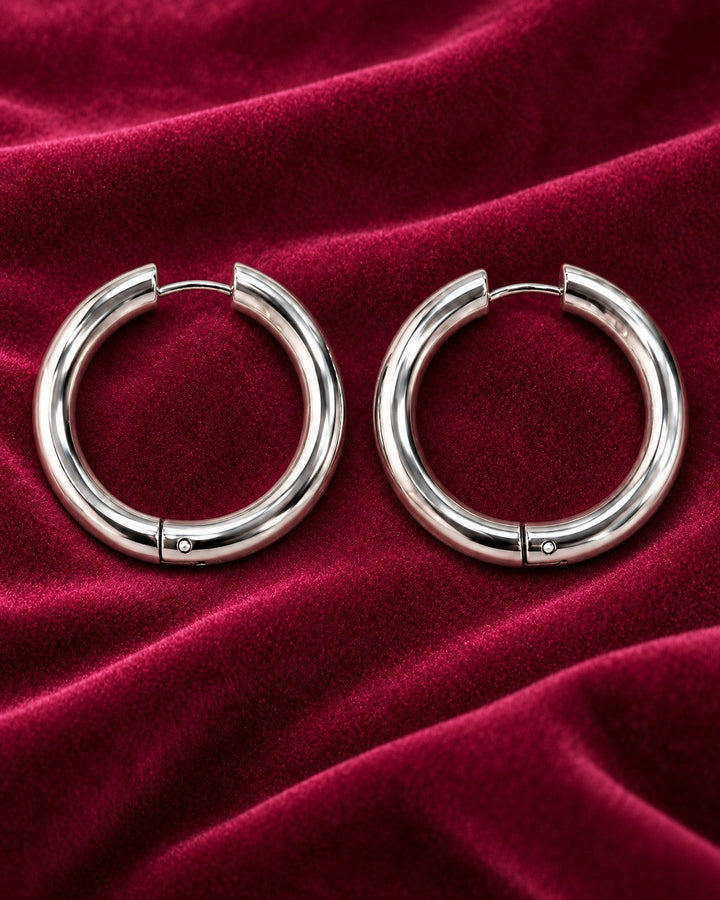 Elli Jewellery rhodium plated mid hoop earrings with a polished silver finish on a deep red velvet background.