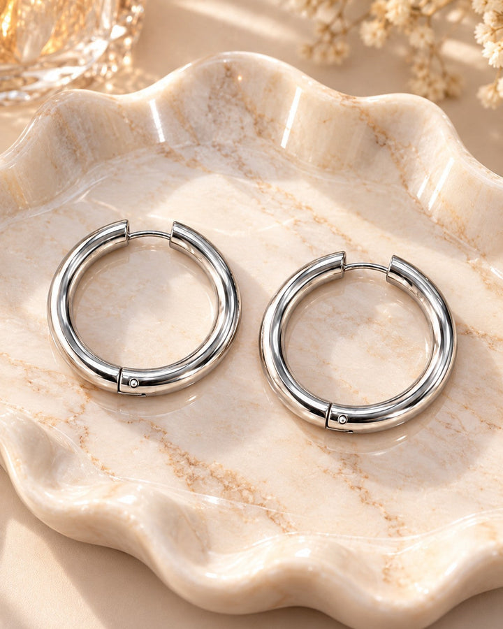 Elli Jewellery rhodium plated mid hoop earrings with a polished silver finish resting on a decorative marble tray.
