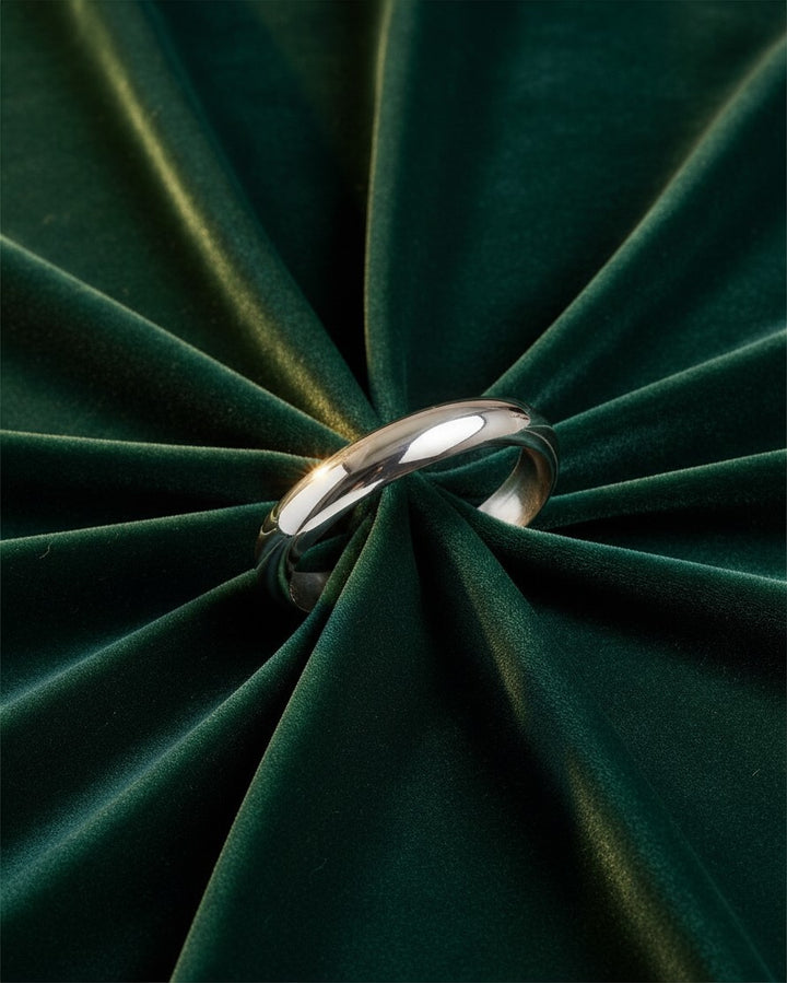 Elli Jewellery rhodium plated polished slim 1cm bangle bracelet resting on a dark green velvet fabric background.