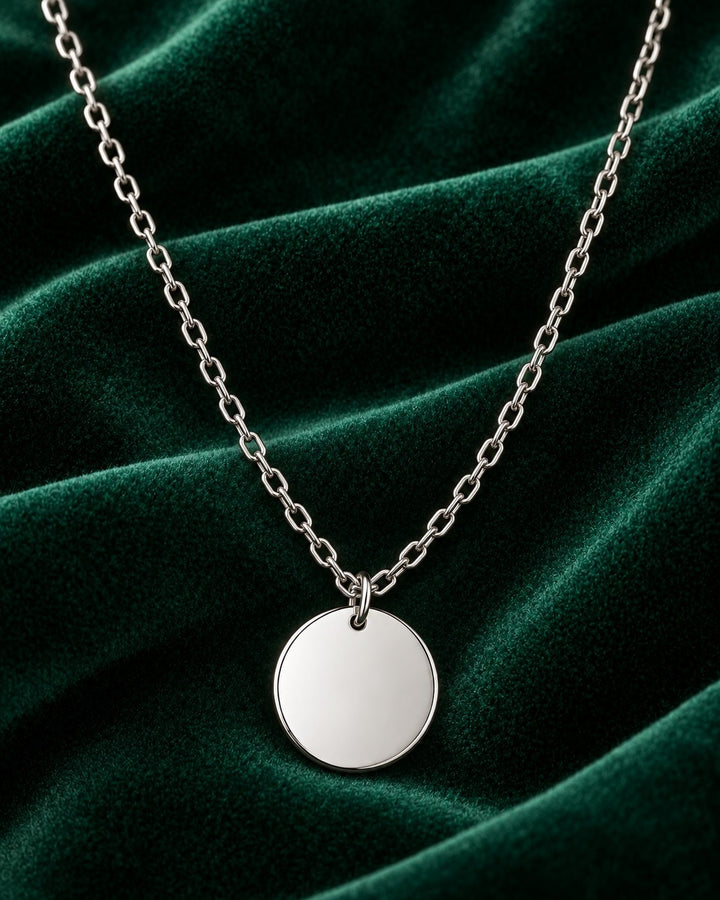 Elli Jewellery rhodium plated minimalist round pendant necklace on a dark green velvet background