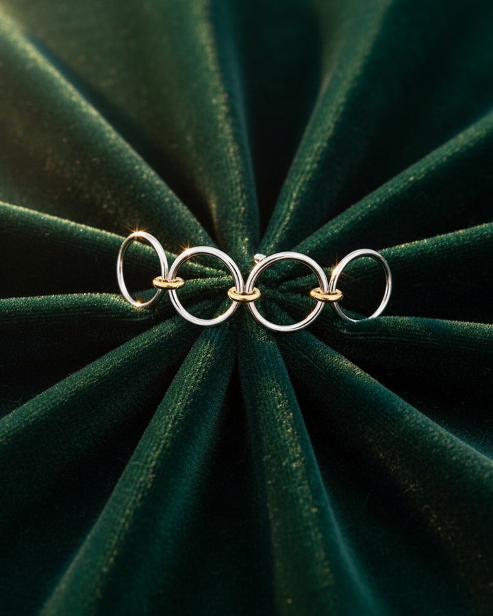 Elli Jewellery rhodium plated multilayer stacking rings with gold-tone accents on a dark green velvet background.