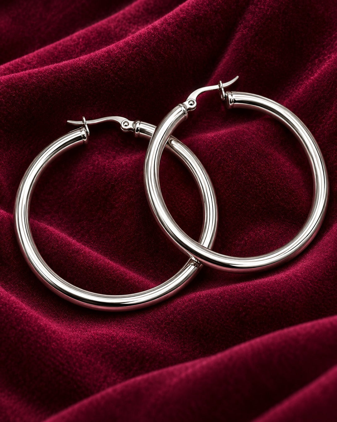 Elli Jewellery 40mm silver hoop earrings with a polished finish resting on a deep red velvet fabric background.