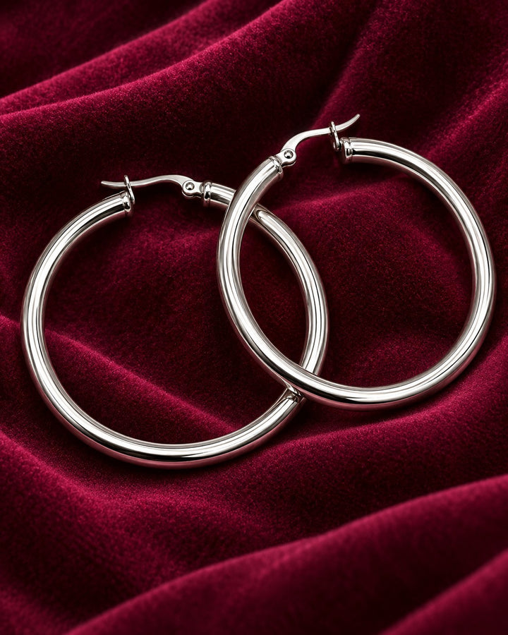 Elli Jewellery 40mm silver hoop earrings with a polished finish resting on a deep red velvet fabric background.