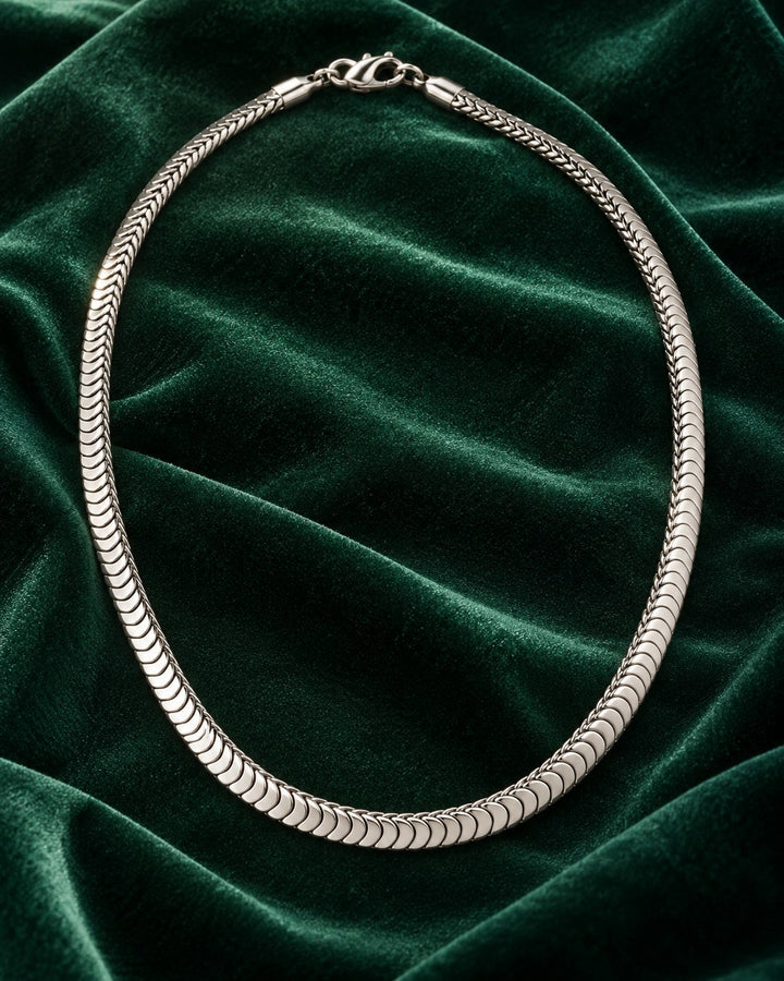 Elli Jewellery silver-toned snake chain necklace with a polished, fluid design resting on dark green velvet fabric.