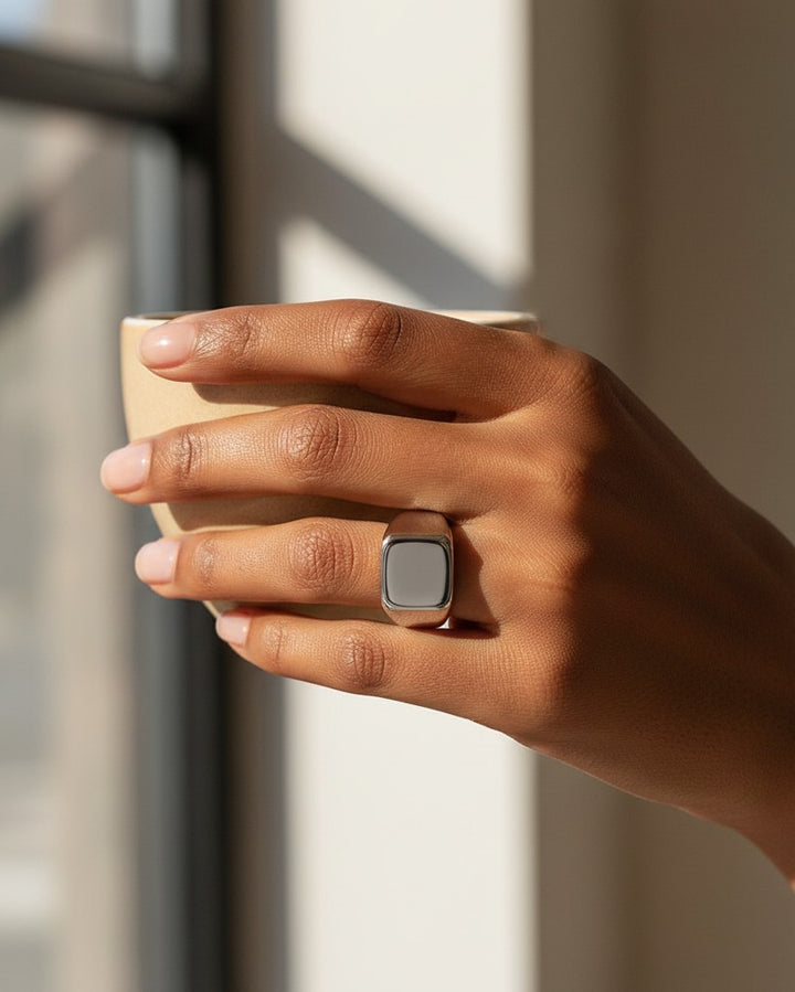 Elli Jewellery silver stainless steel signet ring with a polished finish worn on a hand holding a ceramic cup.