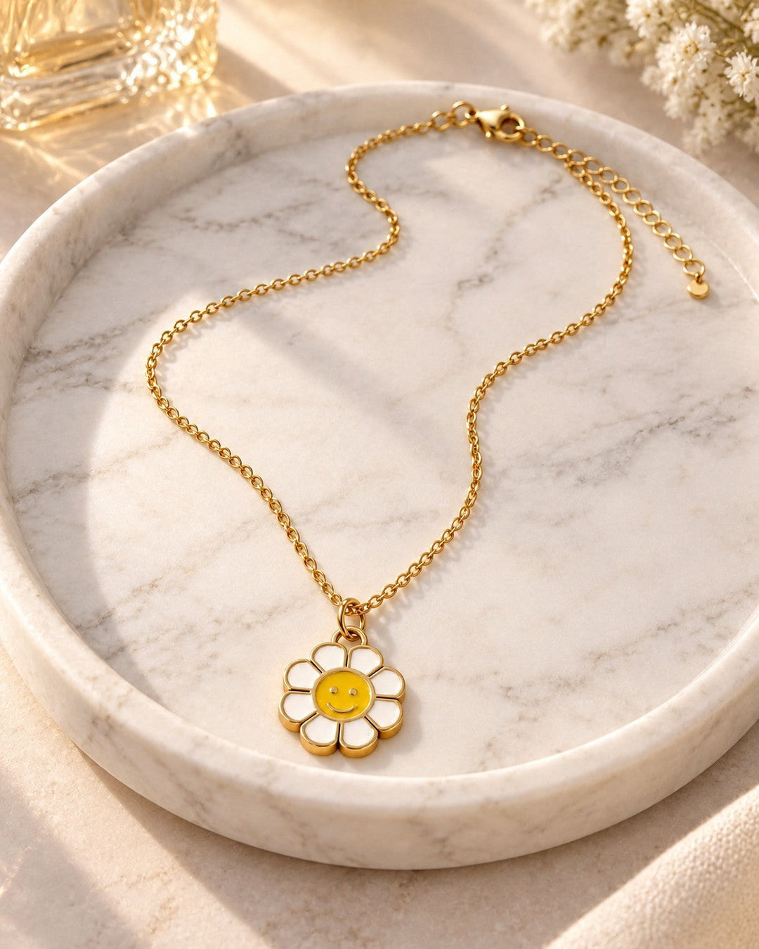 Elli Jewellery gold plated sunflower pendant necklace with a white and yellow smiley face on a marble tray