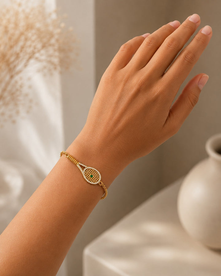 Elli Jewellery gold plated tennis racquet charm bracelet with pavé crystals and a green crystal ball on a wrist