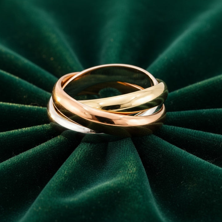 Elli Jewellery Trinity rolling ring featuring three interlocking bands in gold, rose gold, and rhodium on green velvet.