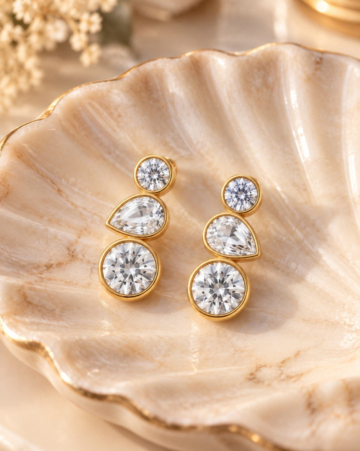 Elli Jewellery triple crystal drop earrings featuring bezel-set cubic zirconia in 18ct gold plated metal on a shell.