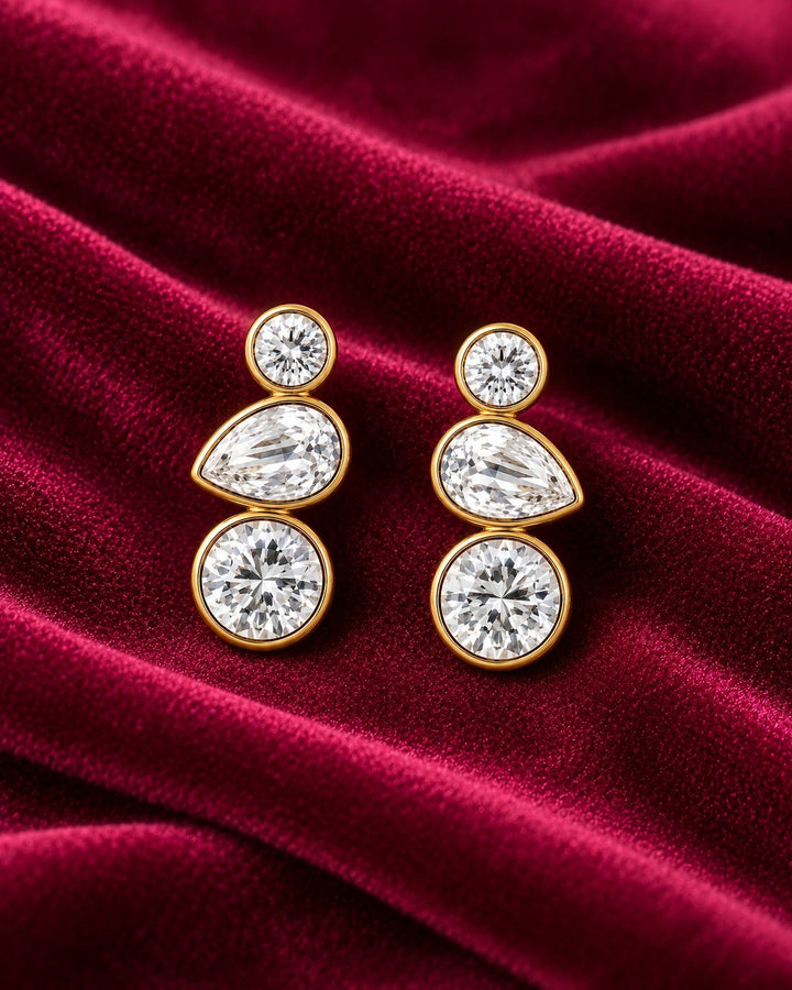 Elli Jewellery triple crystal drop earrings featuring bezel-set cubic zirconia on 18ct gold plated metal on velvet.