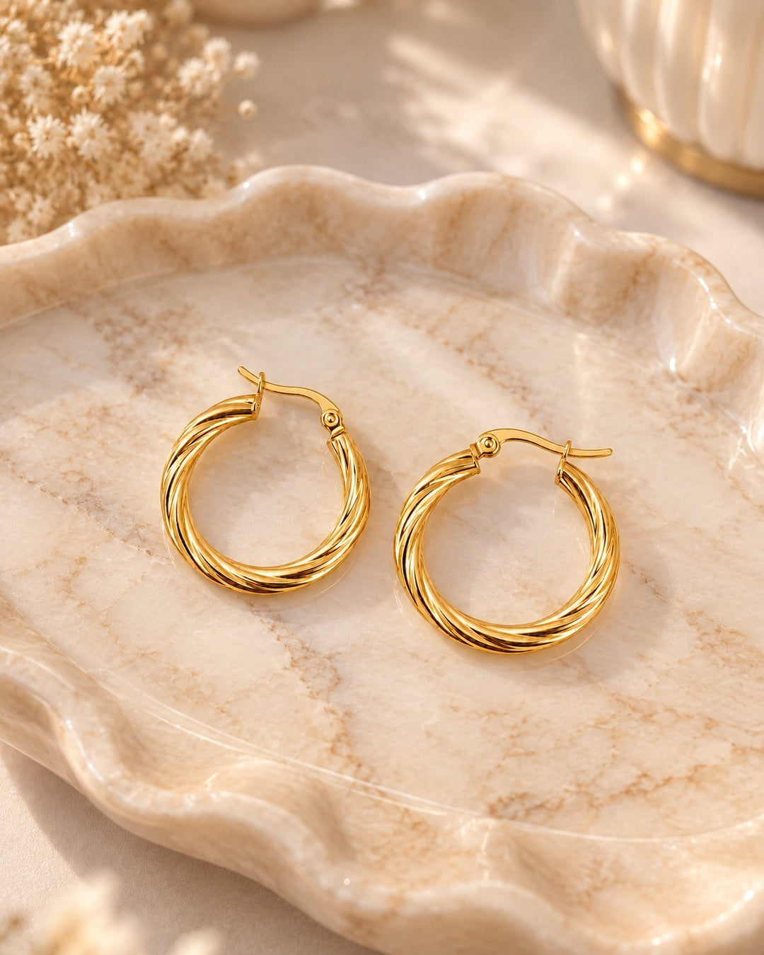 Elli Jewellery gold plated hoop earrings with a twisted rope texture on a decorative marble tray.