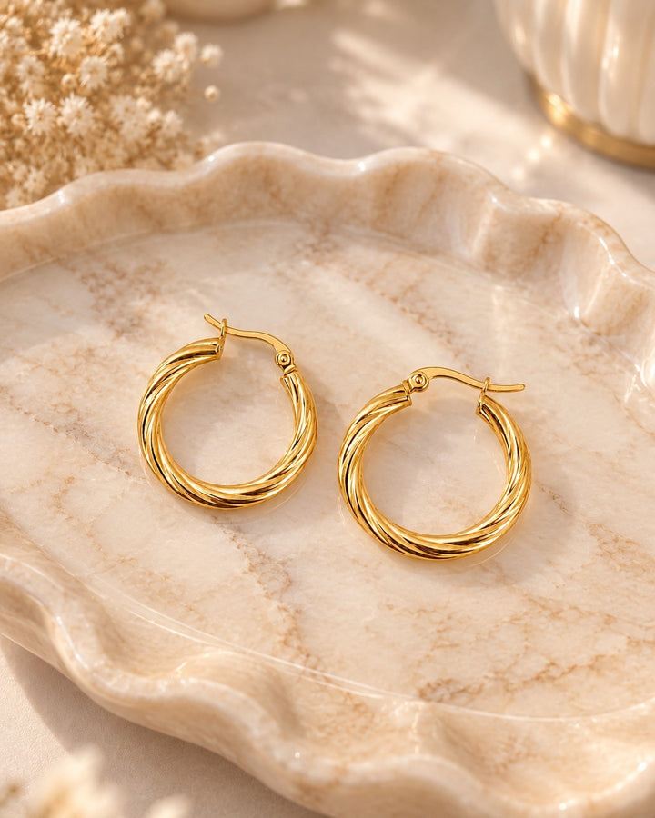 Elli Jewellery gold plated hoop earrings with a twisted rope texture on a decorative marble tray.