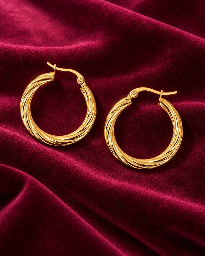 Elli Jewellery gold plated hoop earrings with a twisted rope texture on a luxurious deep red velvet background.