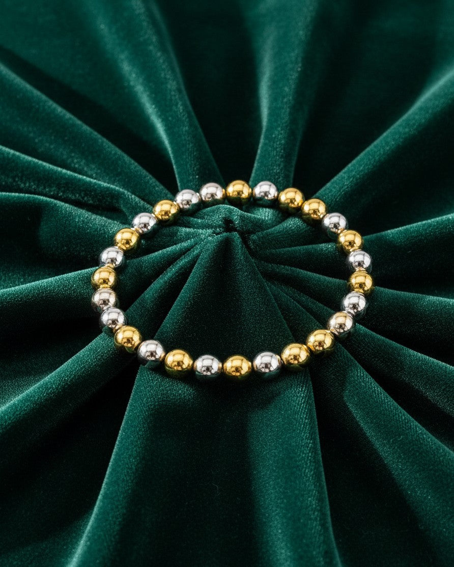 Elli Jewellery two-tone stretch bracelet with alternating gold and silver plated beads on dark green velvet fabric.