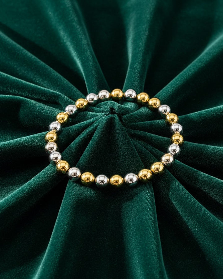 Elli Jewellery two-tone stretch bracelet with alternating gold and silver plated beads on dark green velvet fabric.