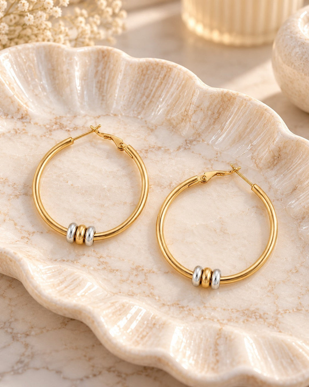Elli Jewellery two-tone hoop earrings with gold plating and rhodium beads resting on a decorative ceramic dish.
