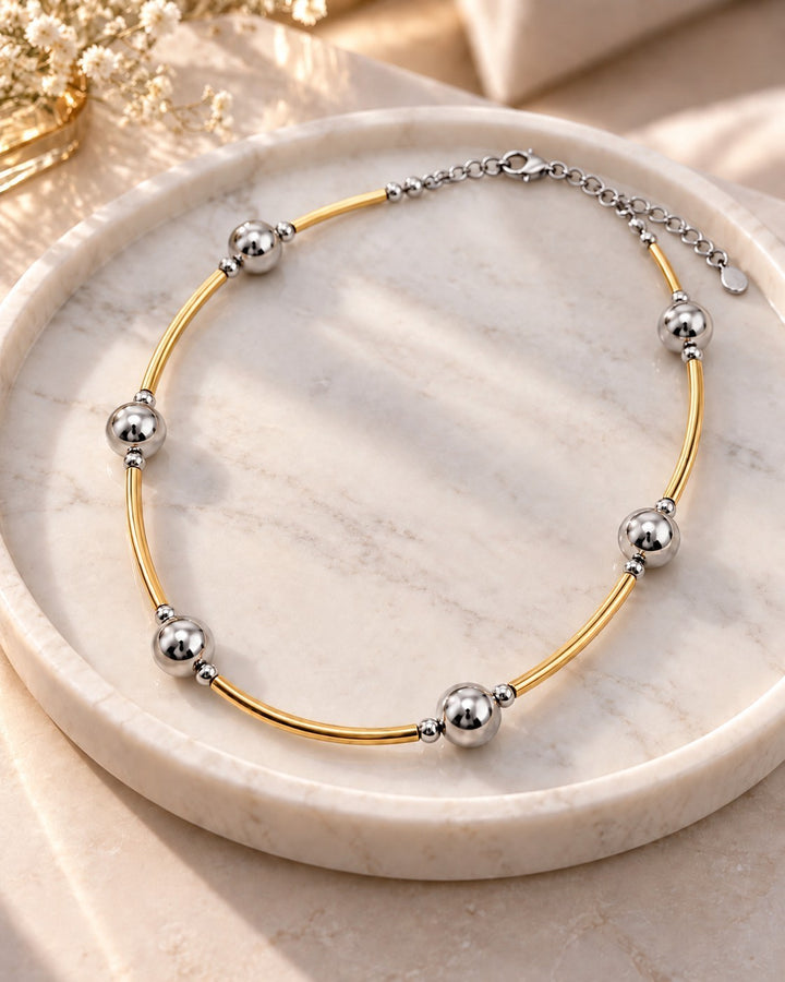 Elli Jewellery two-tone beaded statement necklace featuring gold-plated bars and silver-tone spheres on a marble tray.