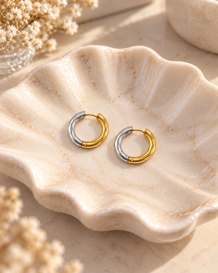 Elli Jewellery two-tone gold and silver 20mm chunky huggie hoop earrings resting in a decorative ceramic shell dish.
