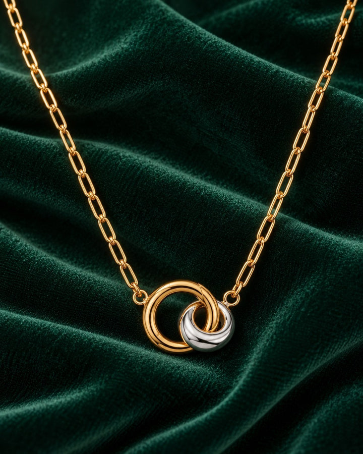 Elli Jewellery two-tone gold and silver geometric link pendant necklace on a dark green velvet background