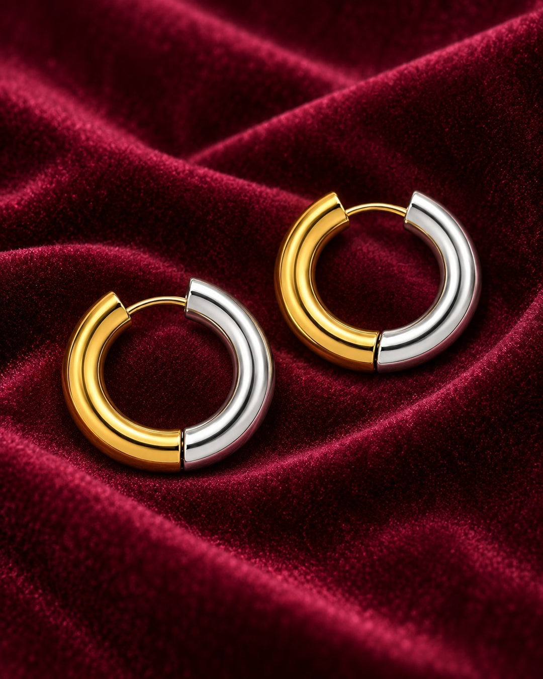 Elli Jewellery two-tone 18mm huggie hoop earrings featuring a polished gold and silver plated finish on red velvet.