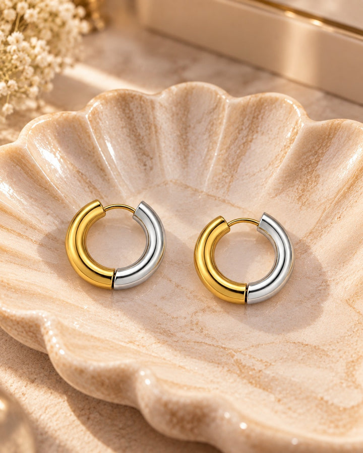 Elli Jewellery two-tone 18mm huggie hoop earrings in gold and silver plating displayed on a decorative shell dish.