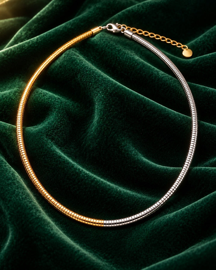 Elli Jewellery two-tone snake chain necklace featuring gold and silver plated links on a dark green velvet background.