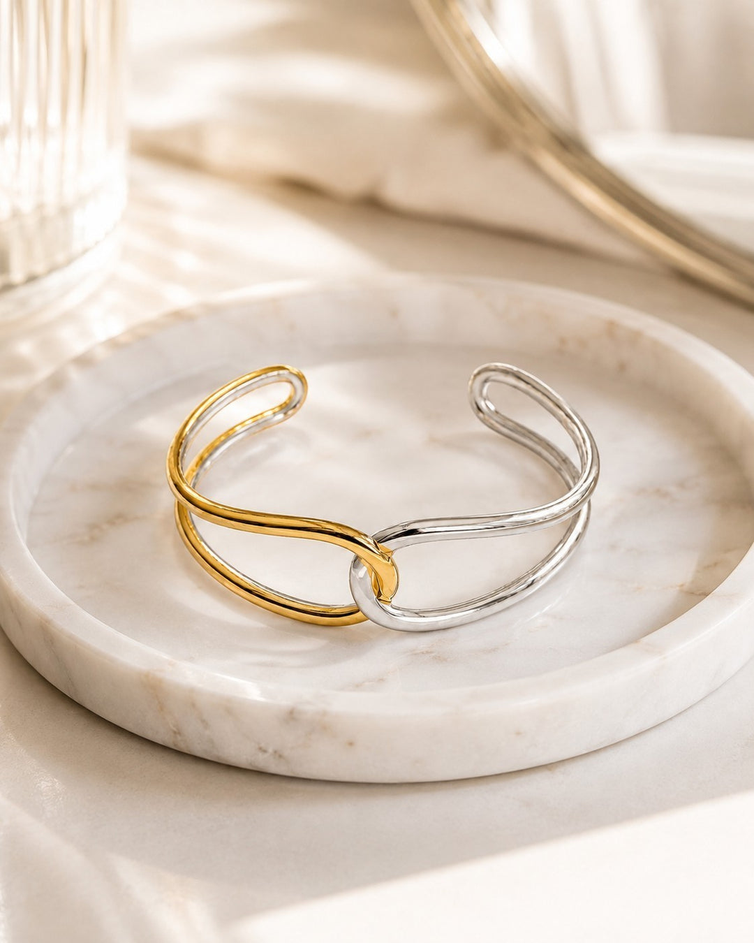 Elli Jewellery two-tone twist bangle bracelet in gold and silver plating resting on a white marble tray.