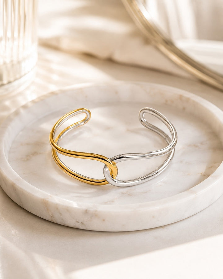 Elli Jewellery two-tone twist bangle bracelet in gold and silver plating resting on a white marble tray.