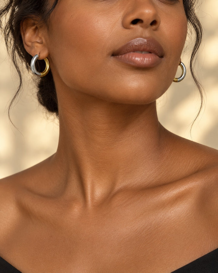 Elli Jewellery two-toned gold and silver chunky huggie hoop earrings worn by a model with a minimalist aesthetic.