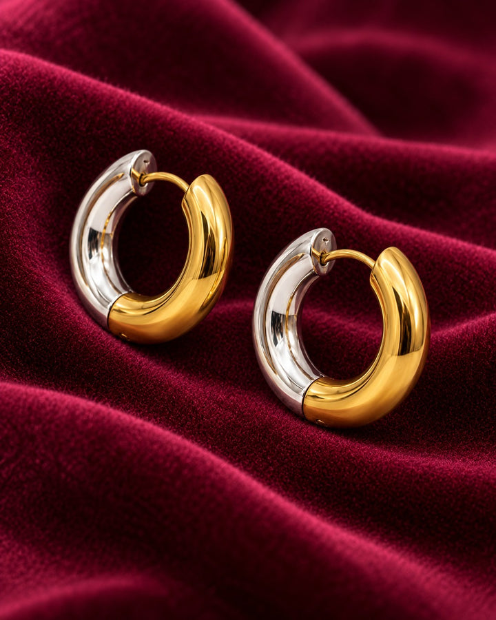Elli Jewellery chunky 24mm huggie hoop earrings in polished two-toned gold and silver plating on red velvet fabric.