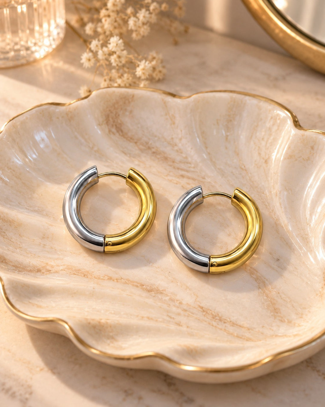 Elli Jewellery two-toned gold and silver 24mm chunky huggie hoop earrings resting on a decorative shell dish.