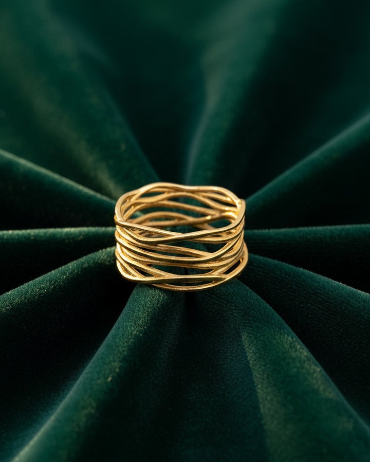 Elli Jewellery wide gold plated band ring featuring an intricate woven reed pattern on a dark green velvet background.